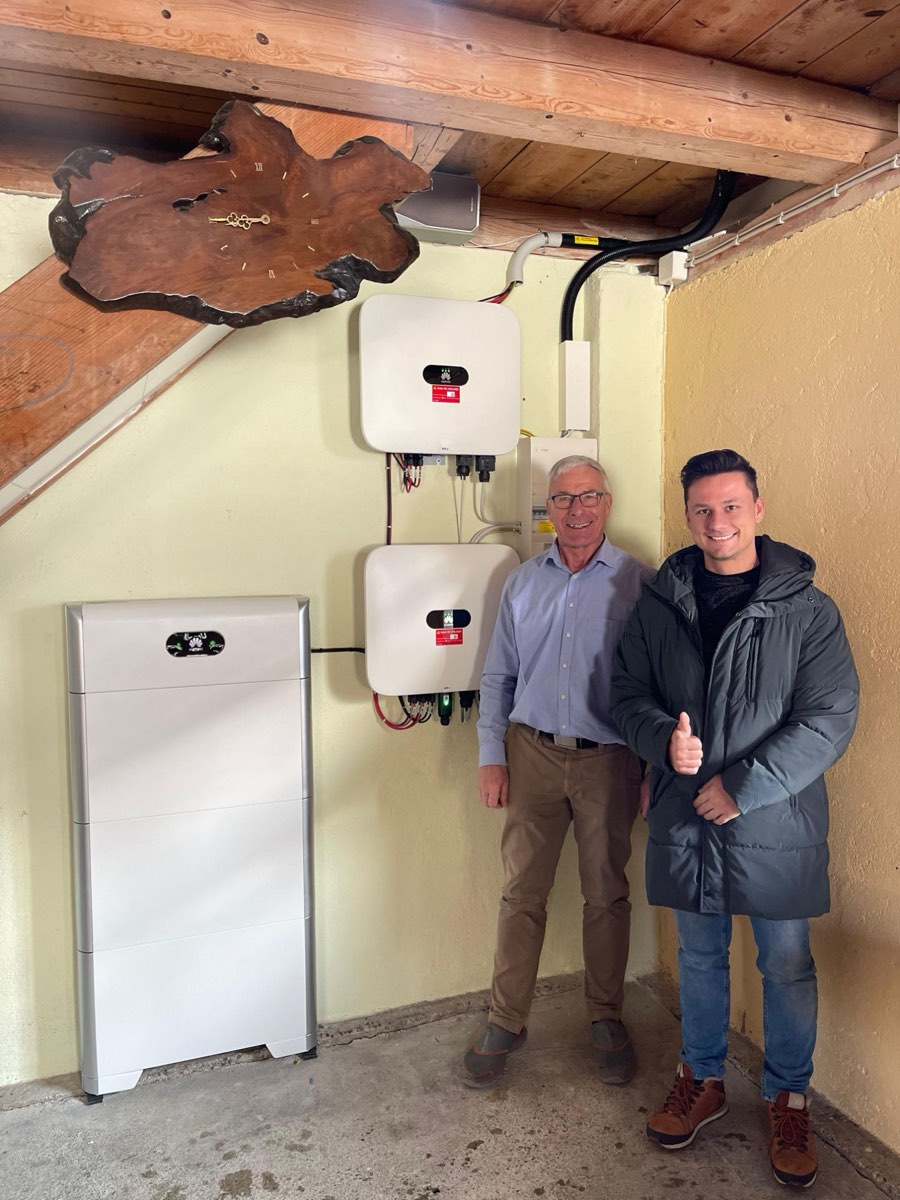 Hans Grossenbacher aus Dürrenäsch AG mit Runer-Berater vor dem frisch installierten Batteriespeicher und zwei Wechselrichtern — Daumen hoch